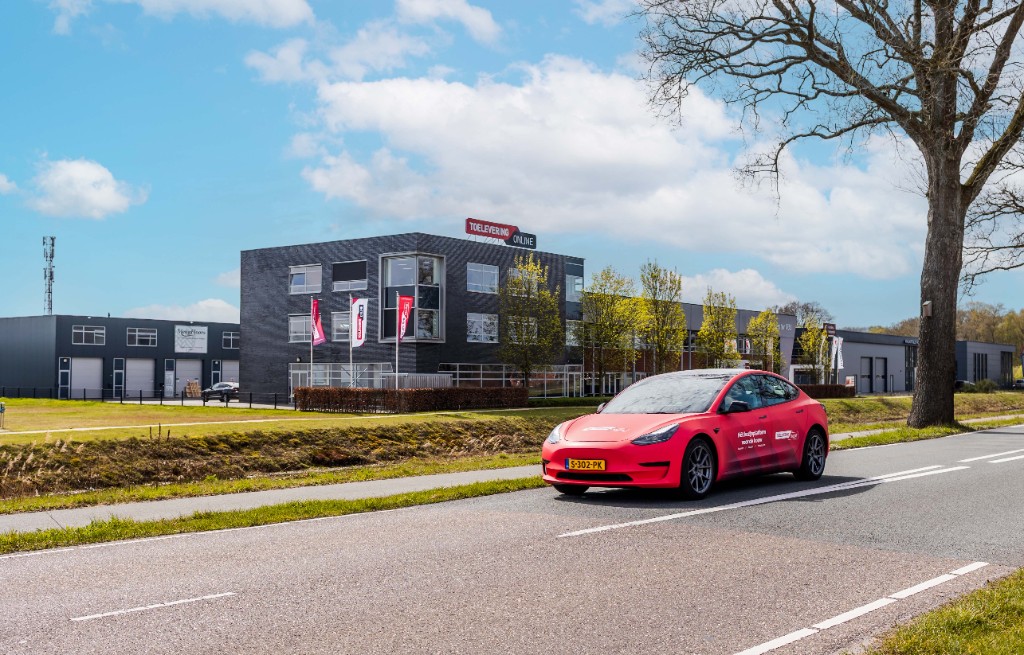 Red Toelevering Online branded car parked in front of the company headquarters building on a sunny day